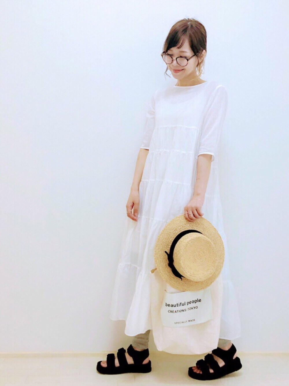 ホワイト系のワンピース、ホワイト系のトートバッグ、ブラック系のサンダルを着用したレディースの夏コーディネートの1枚目の写真