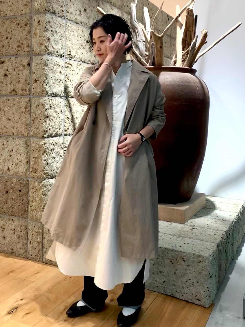 ベージュ系のステンカラーコート、ホワイト系のワンピース、ブルー系のデニムパンツを着用したレディースの冬コーディネートの1枚目の写真