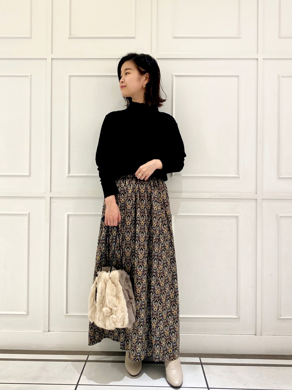 ブラック系のニット/セーター、ブラック系のスカート、ベージュ系のトートバッグを着用したレディースの秋コーディネートの1枚目の写真