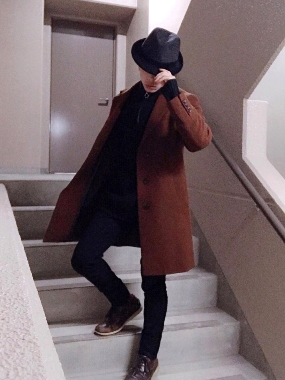 ブラウン系のチェスターコート、ブラック系のニット/セーター、ブラック系のパンツを着用したメンズの冬コーディネートの1枚目の写真