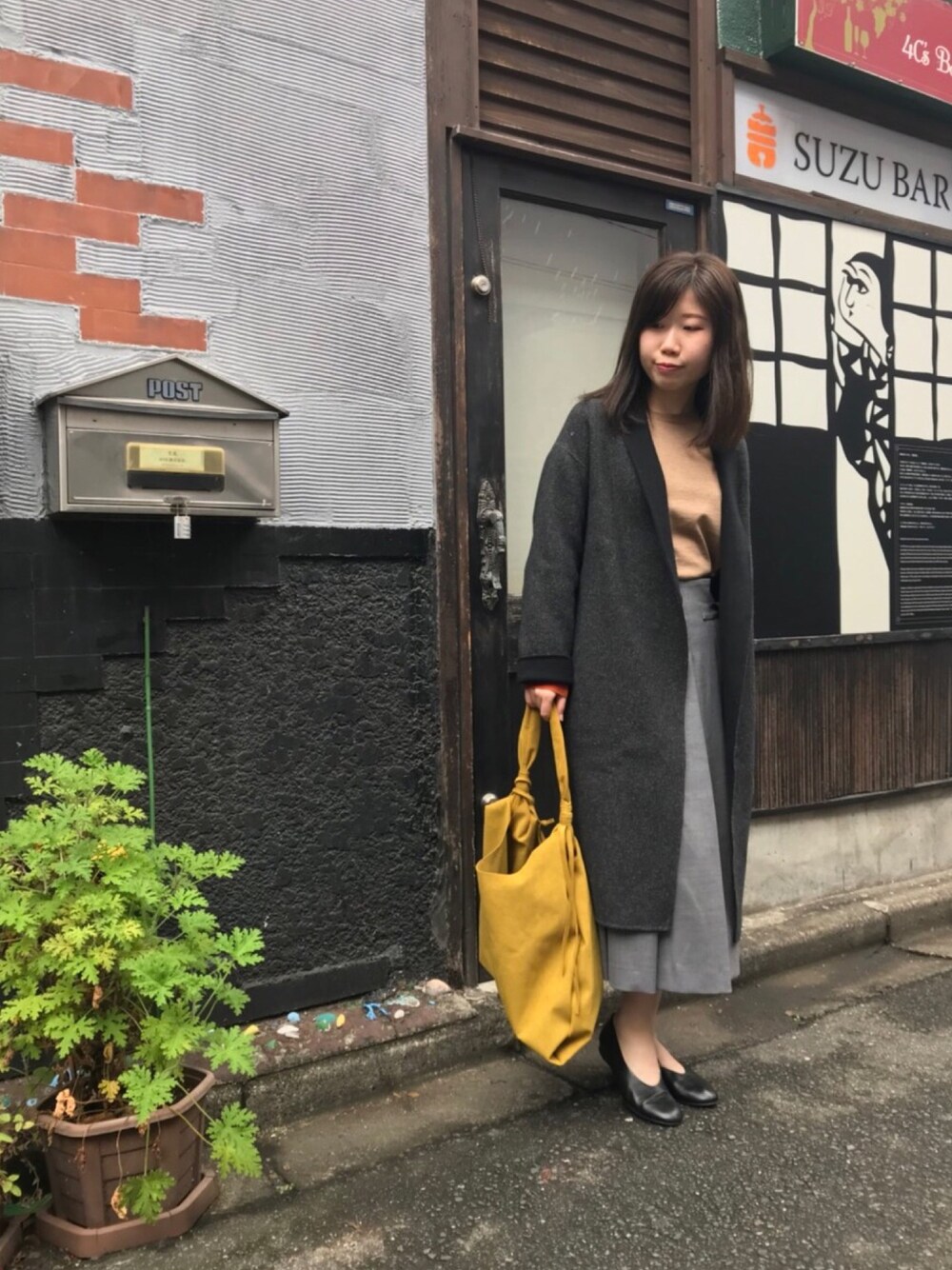 ブラック系のチェスターコート、イエロー系のニット/セーター、グレー系のスカートを着用したレディースの秋コーディネートの1枚目の写真