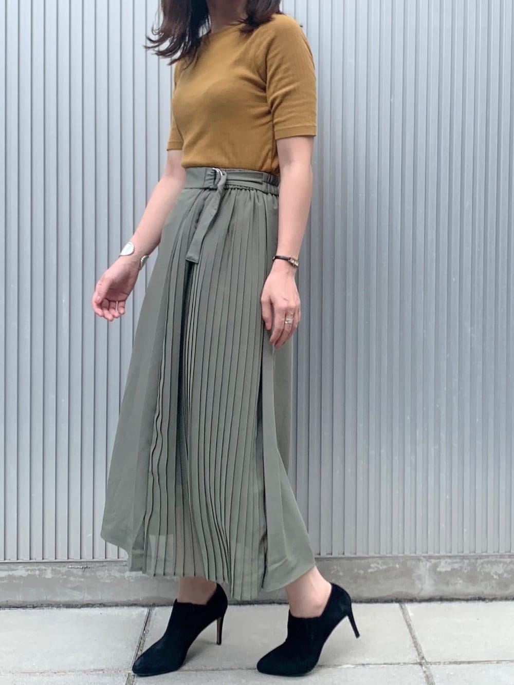 イエロー系のトップス、グリーン系のスカート、ブラック系のブーティを着用したレディースの秋コーディネートの1枚目の写真