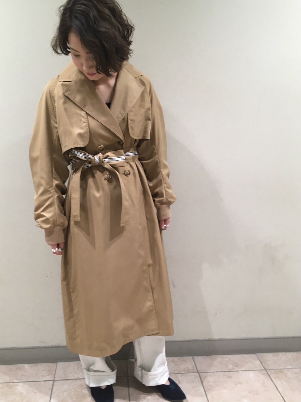 ベージュ系のトレンチコート、ホワイト系のデニムパンツ、グリーン系のパンプスを着用したレディースの冬コーディネートの1枚目の写真