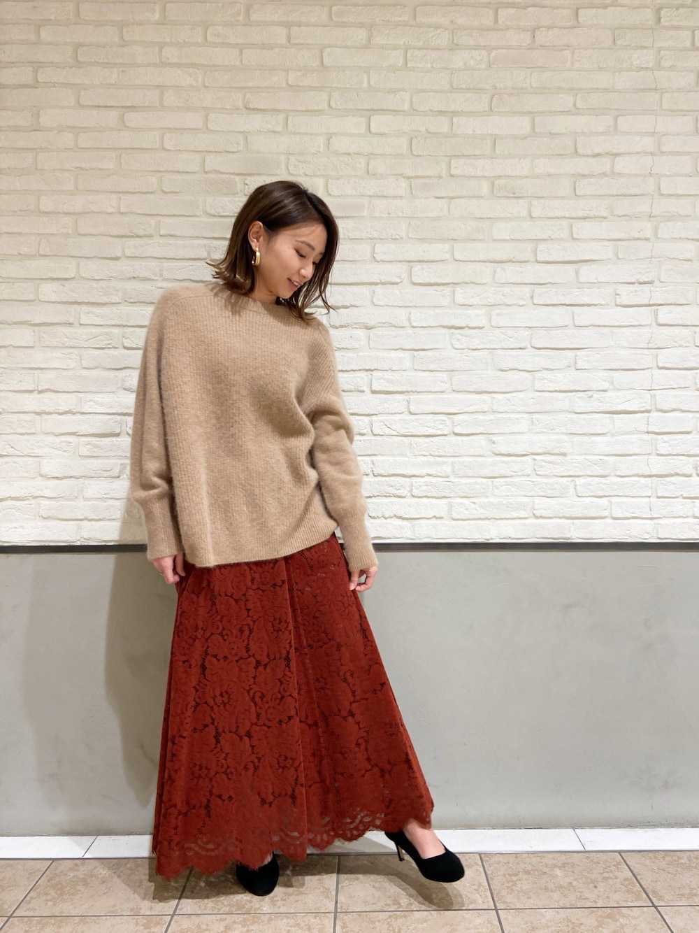 ベージュ系のニット/セーター、オレンジ系のスカート、ブラック系のパンプスを着用したレディースの冬コーディネートの1枚目の写真