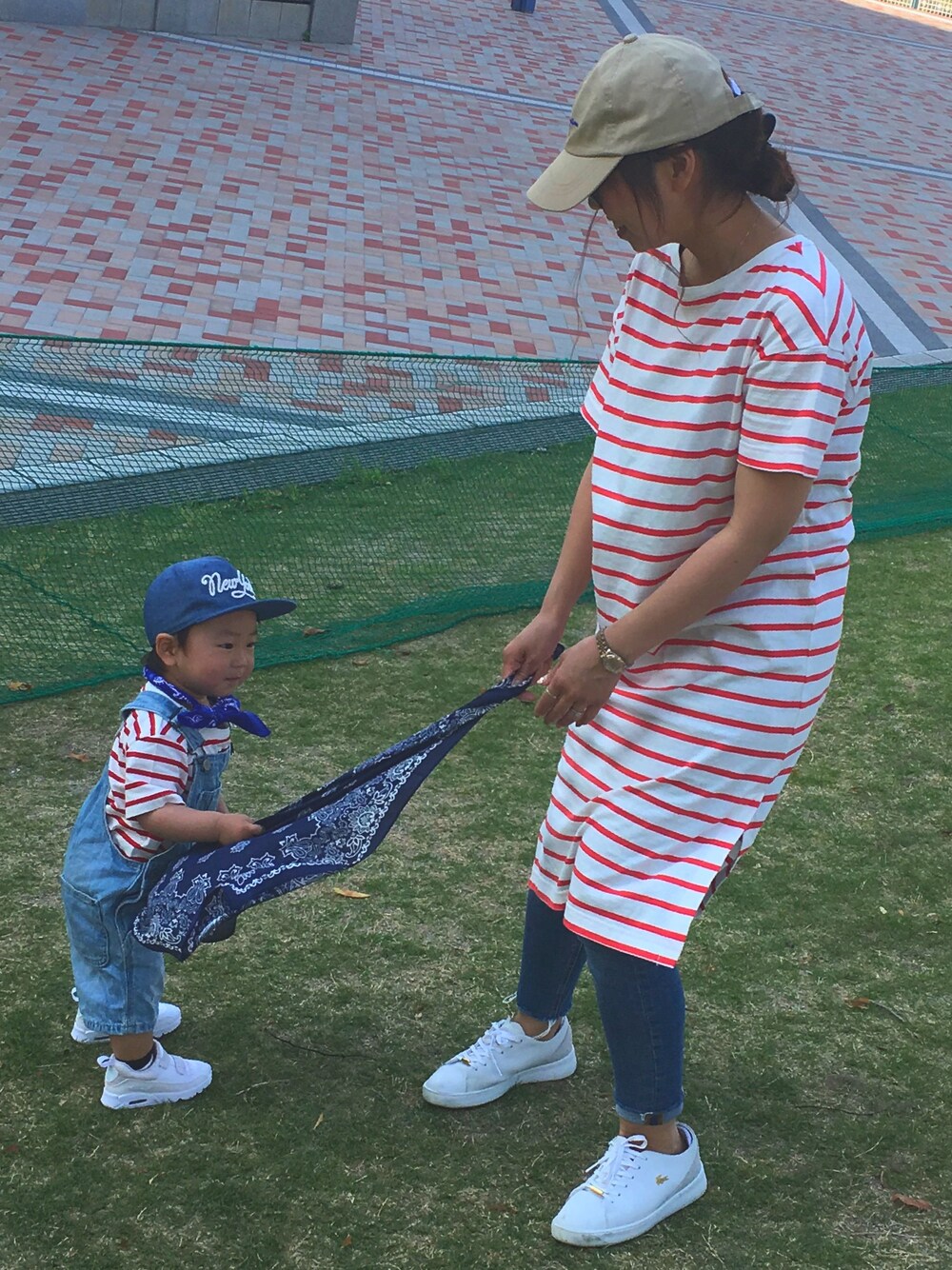 レッド系のワンピース、ブルー系のデニムパンツ、ホワイト系のスニーカーを着用したレディースの春コーディネートの1枚目の写真