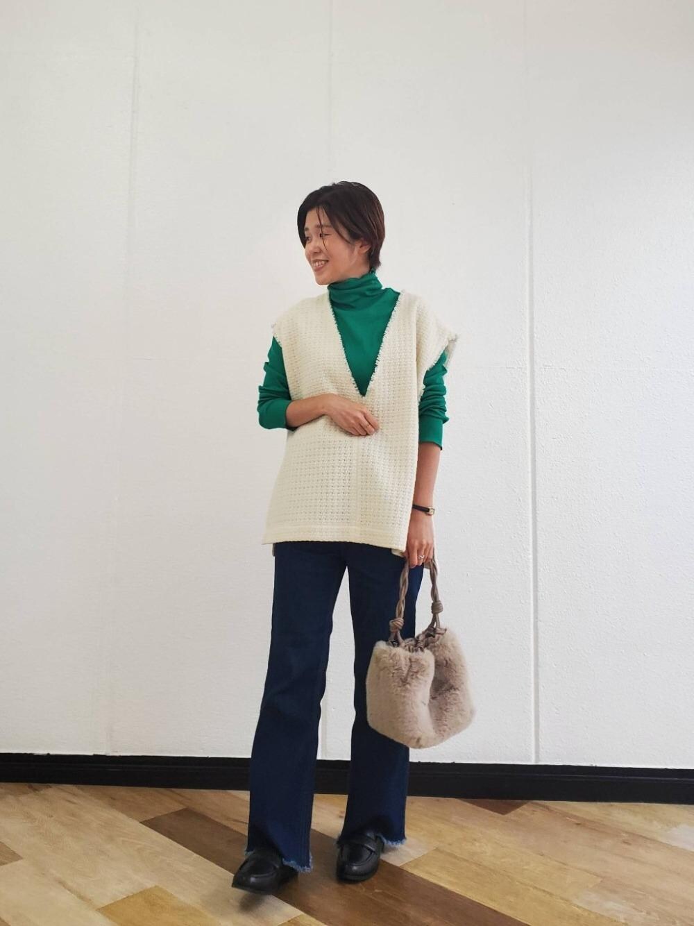 ブルー系のデニムパンツ、ベージュ系のショルダーバッグ、ホワイト系のベストを着用したレディースの秋コーディネートの1枚目の写真