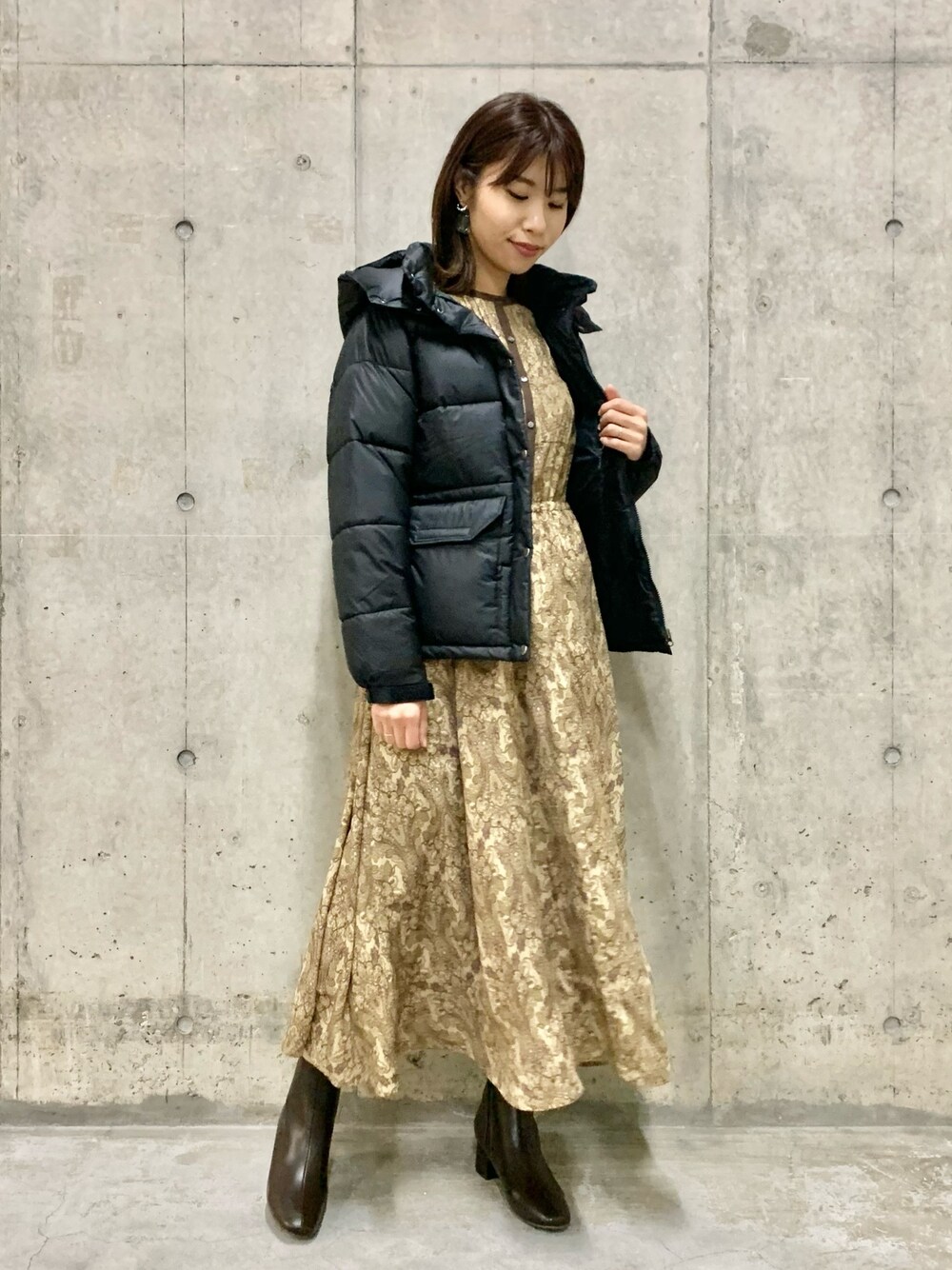 ベージュ系のワンピース、ブラック系のダウンジャケット/コート、ブラウン系のブーツを着用したレディースの冬コーディネートの1枚目の写真