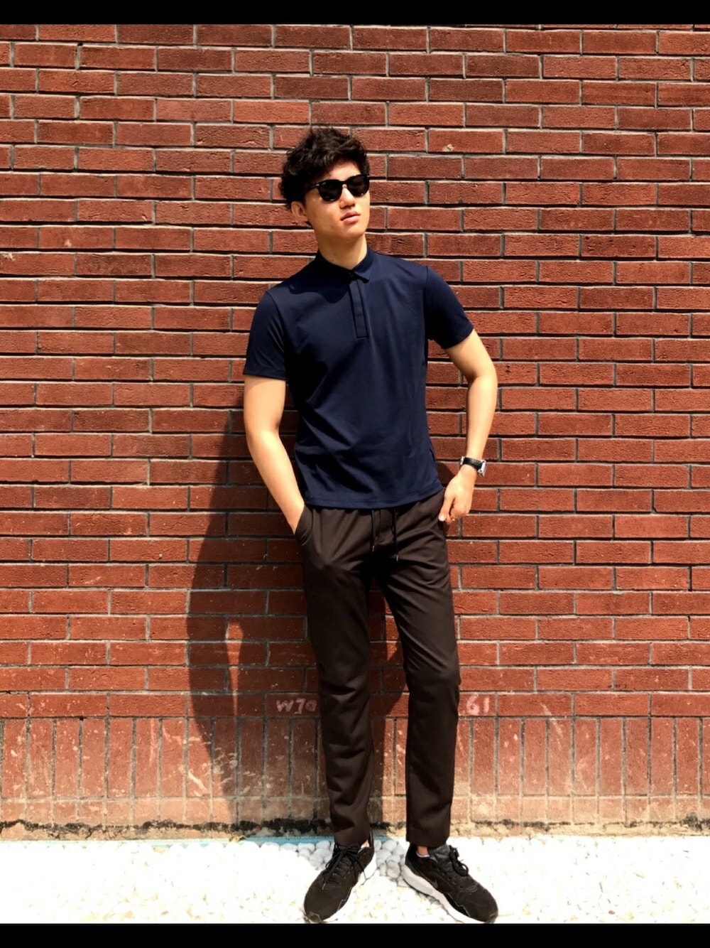 ブルー系のポロシャツ、ブラウン系のスラックス、ブラック系のスニーカーを着用したメンズの春コーディネートの1枚目の写真