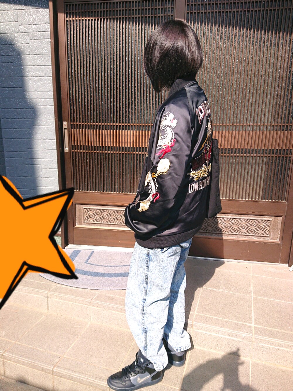 ブラック系のスカジャン、ブルー系のデニムパンツ、ブラック系のスニーカーを着用したレディースの秋コーディネートの1枚目の写真