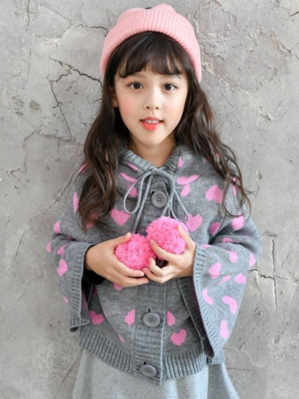 「アウター、ガーリー、ハート、韓国子供服、女の子、ポンポン、秋冬コーデ、おしゃれさんと繋がりたい、子供服Bee」｜「Bee des Beeのポンポン付き　ハート柄 ニットポンチョ（ポンチョ、グレー系）」を使った、子供服Beeさん（キッズ・115cm）の冬コーディネートの1枚目の写真