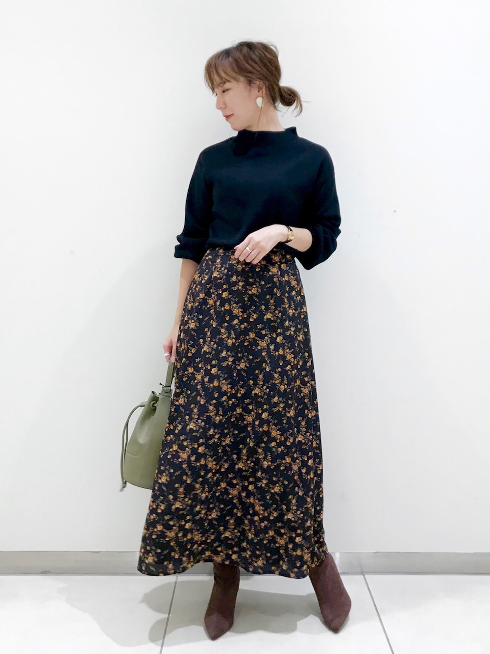 ブラック系のニット/セーター、ブラック系のスカート、グリーン系のショルダーバッグを着用したレディースの秋コーディネートの1枚目の写真