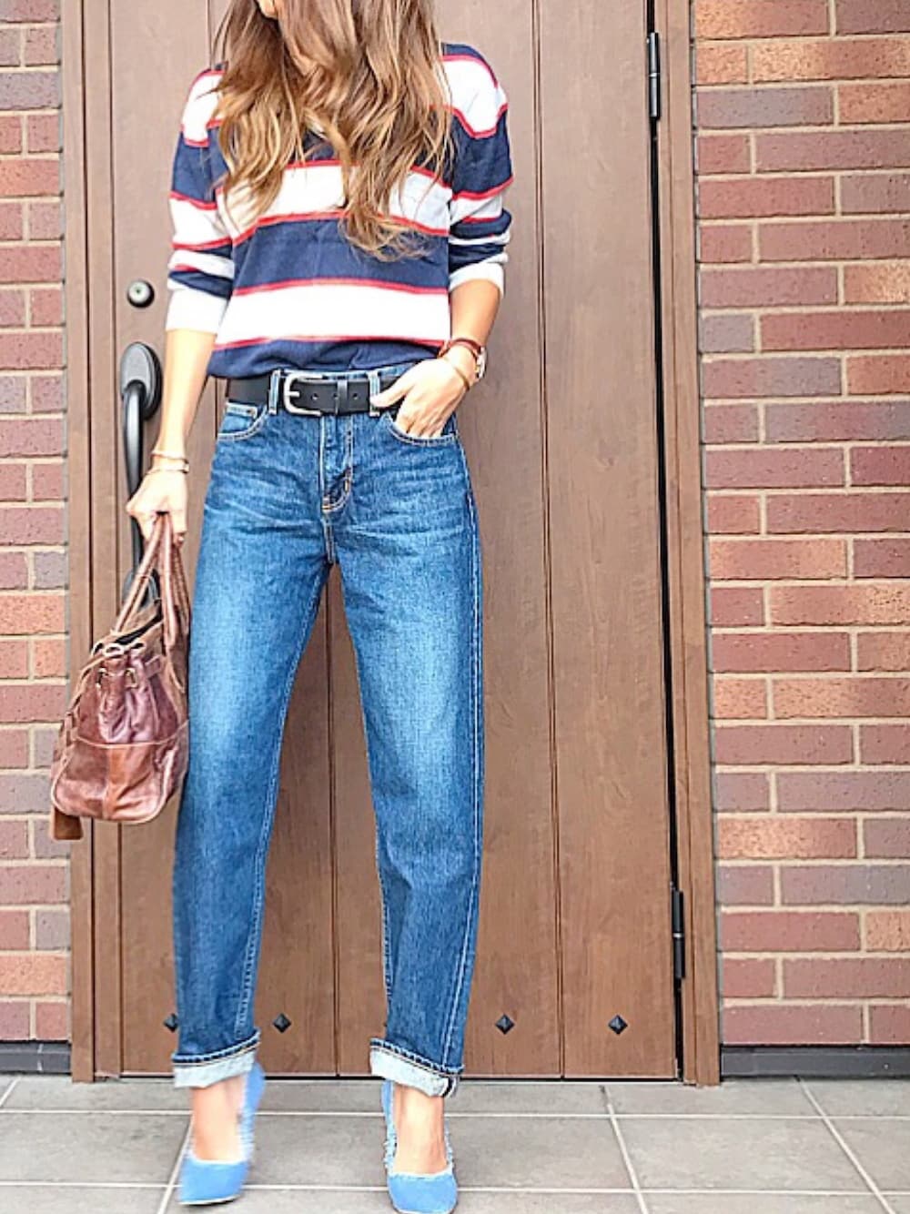 ブルー系のデニムパンツ、ブラウン系のハンドバッグ、ブルー系のトップスを着用したレディースの冬コーディネートの1枚目の写真