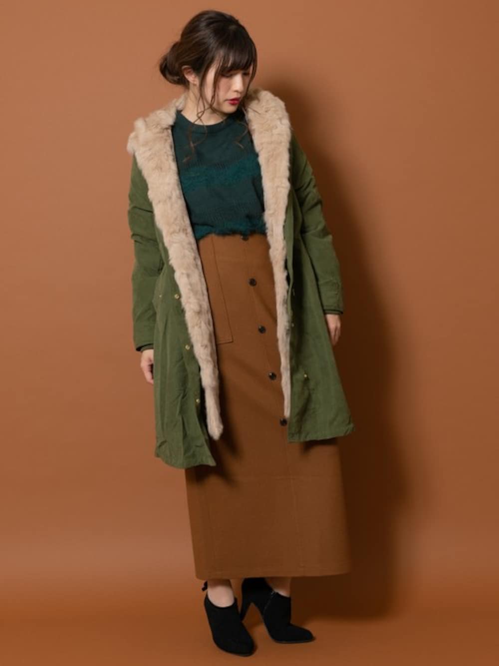 グリーン系のモッズコート、グリーン系のニット/セーター、ブラウン系のスカートを着用したレディースの秋コーディネートの1枚目の写真