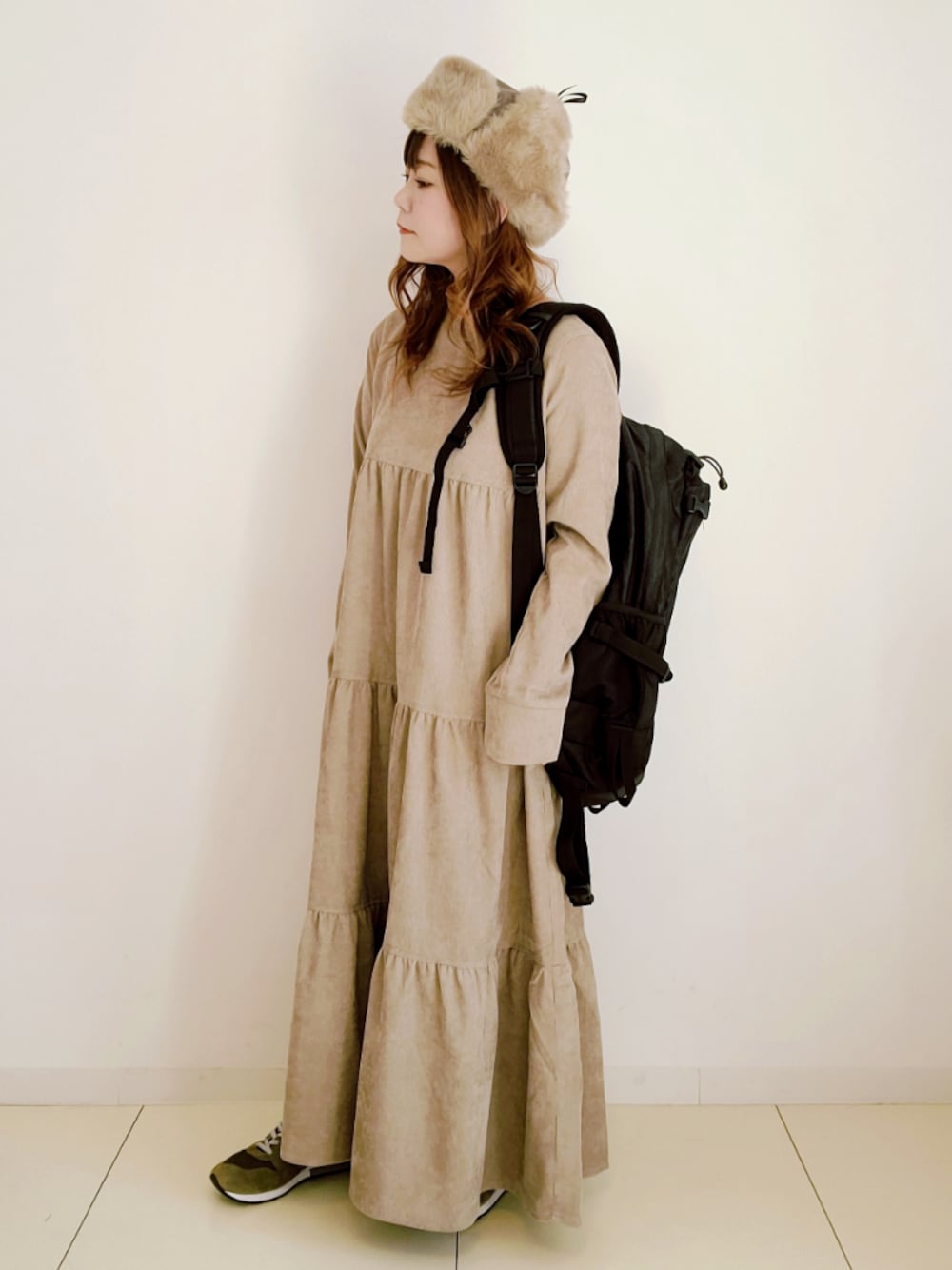 ベージュ系のワンピース、ブラック系のバックパック/リュック、グリーン系のスニーカーを着用したレディースの秋コーディネートの1枚目の写真