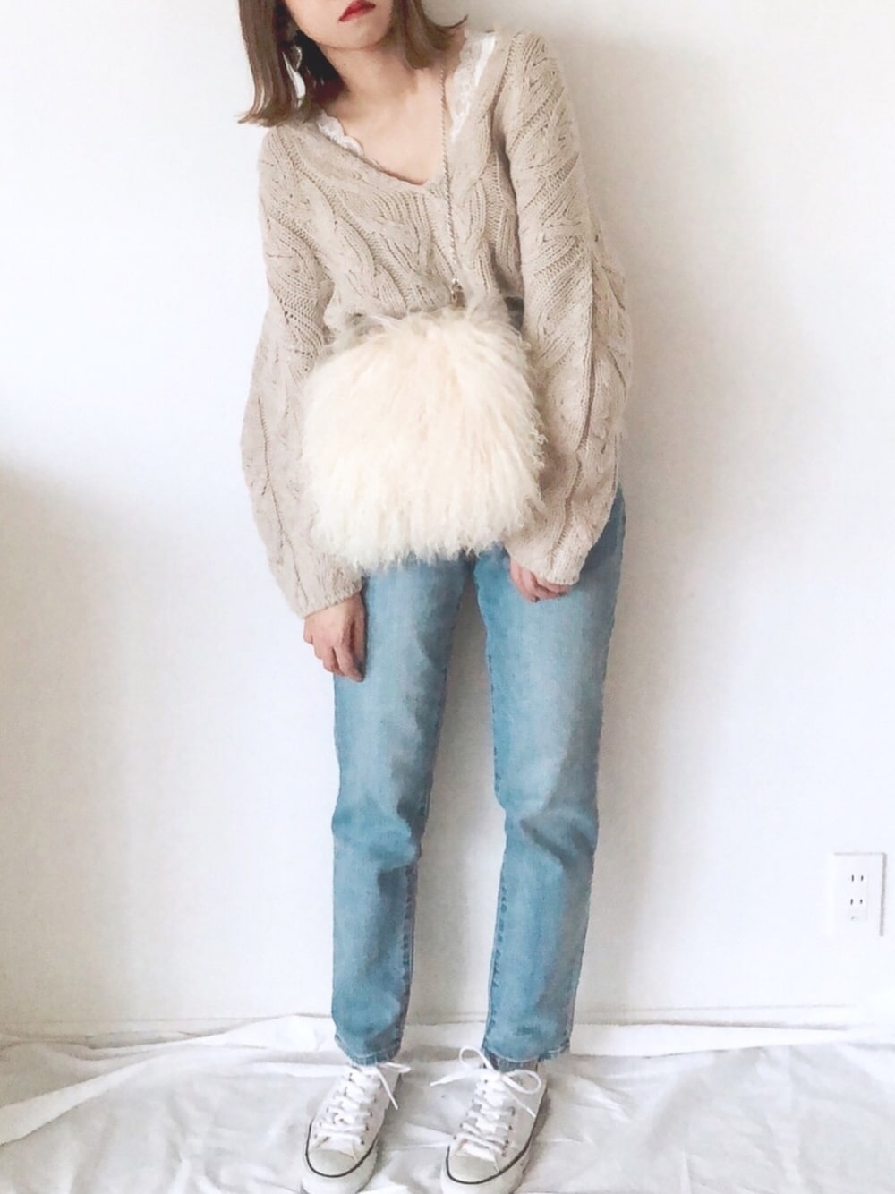 ベージュ系のニット/セーター、ベージュ系のクラッチバッグ、ブルー系のデニムパンツを着用したレディースの秋コーディネートの1枚目の写真