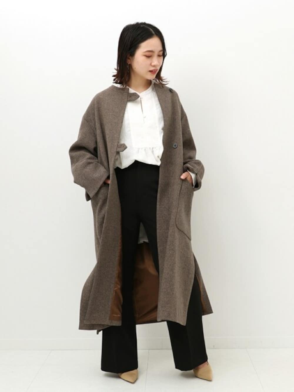 ブラウン系のノーカラーコート、ホワイト系のTシャツ/カットソー、ブラック系のスラックスを着用したレディースの冬コーディネートの1枚目の写真