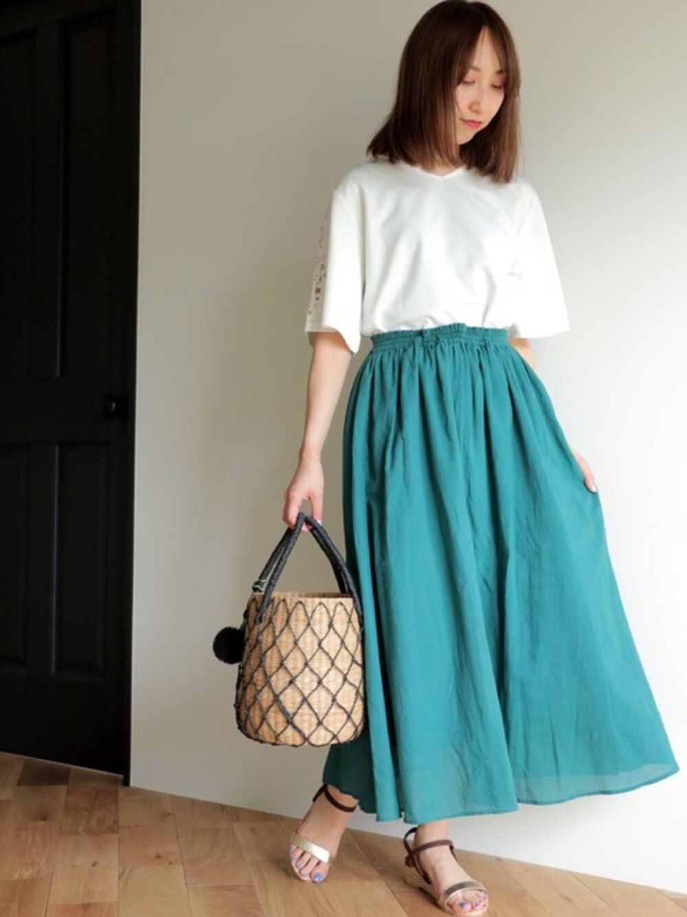 グリーン系のスカート、ホワイト系のTシャツ/カットソー、ブラック系のかごバッグを着用したレディースの夏コーディネートの1枚目の写真