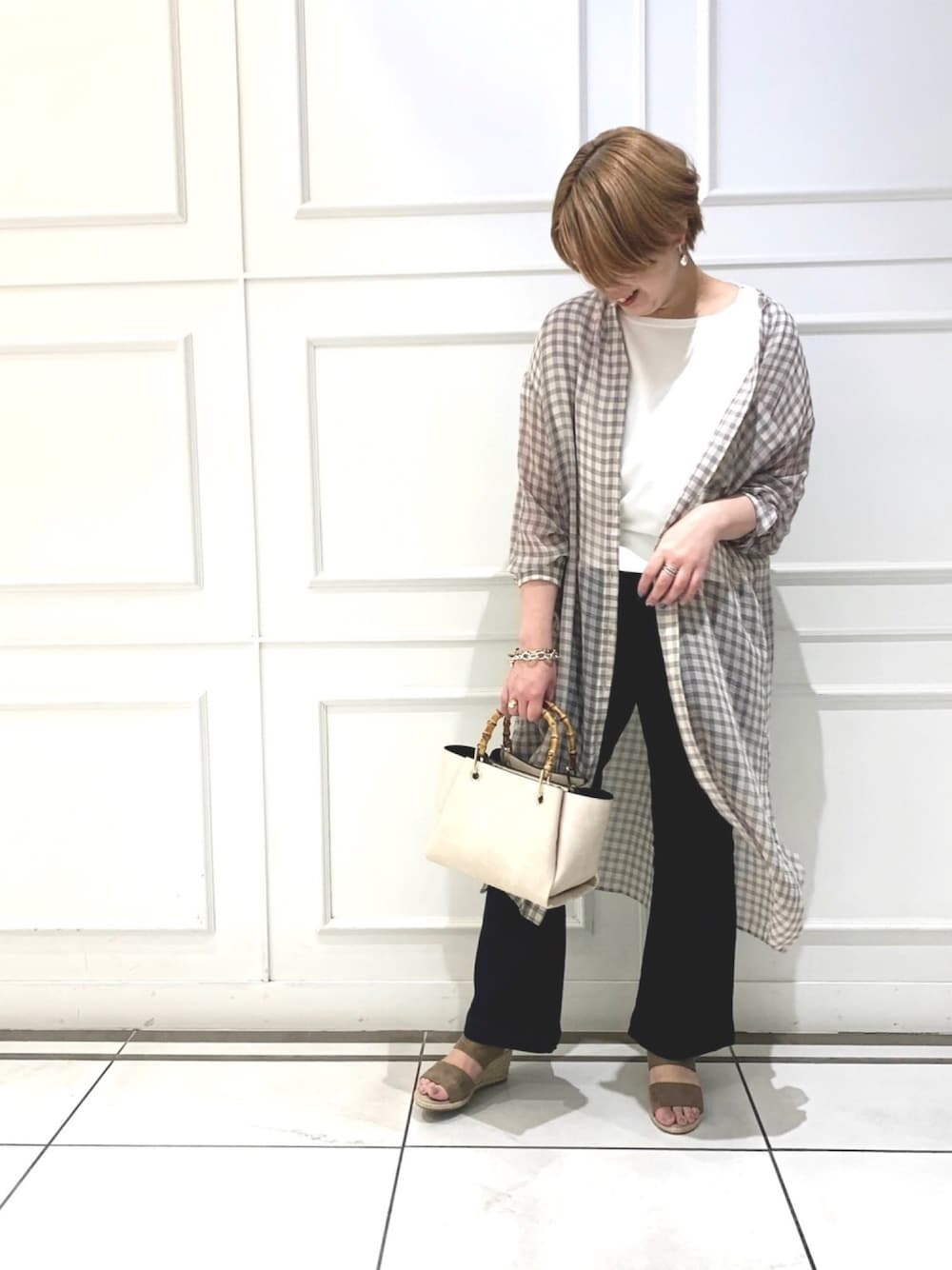 ホワイト系のシャツワンピース、ブルー系のデニムパンツ、ベージュ系のサンダルを着用したレディースの春コーディネートの1枚目の写真