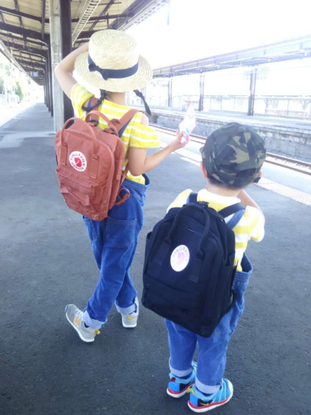 ブラウン系のバックパック/リュック、イエロー系のTシャツ/カットソー、ブルー系のサロペット/オーバーオールを着用したキッズの春コーディネートの1枚目の写真