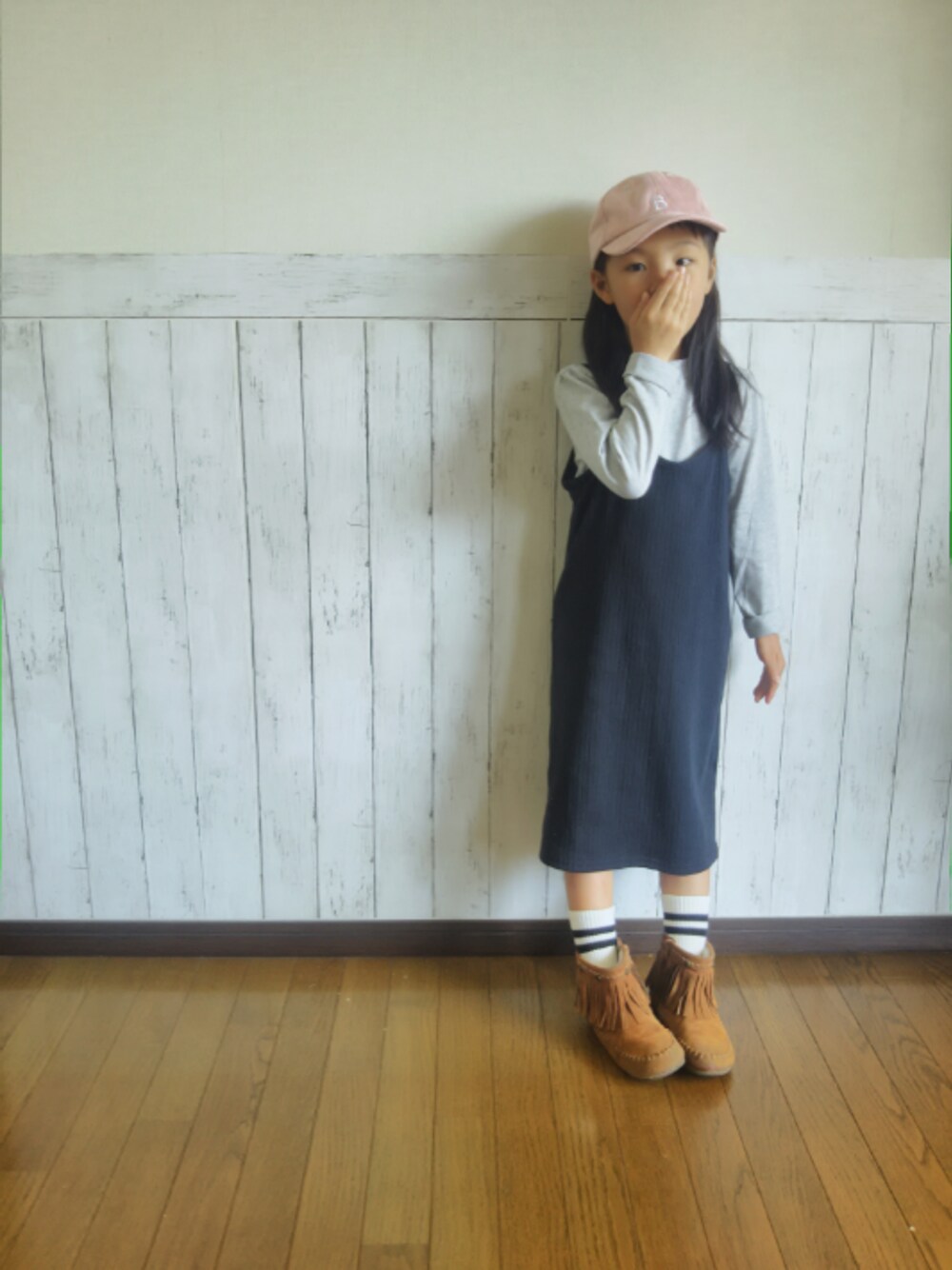 ブラック系のワンピース、ブラウン系のブーツ、ピンク系のキャップを着用したキッズの秋コーディネートの1枚目の写真