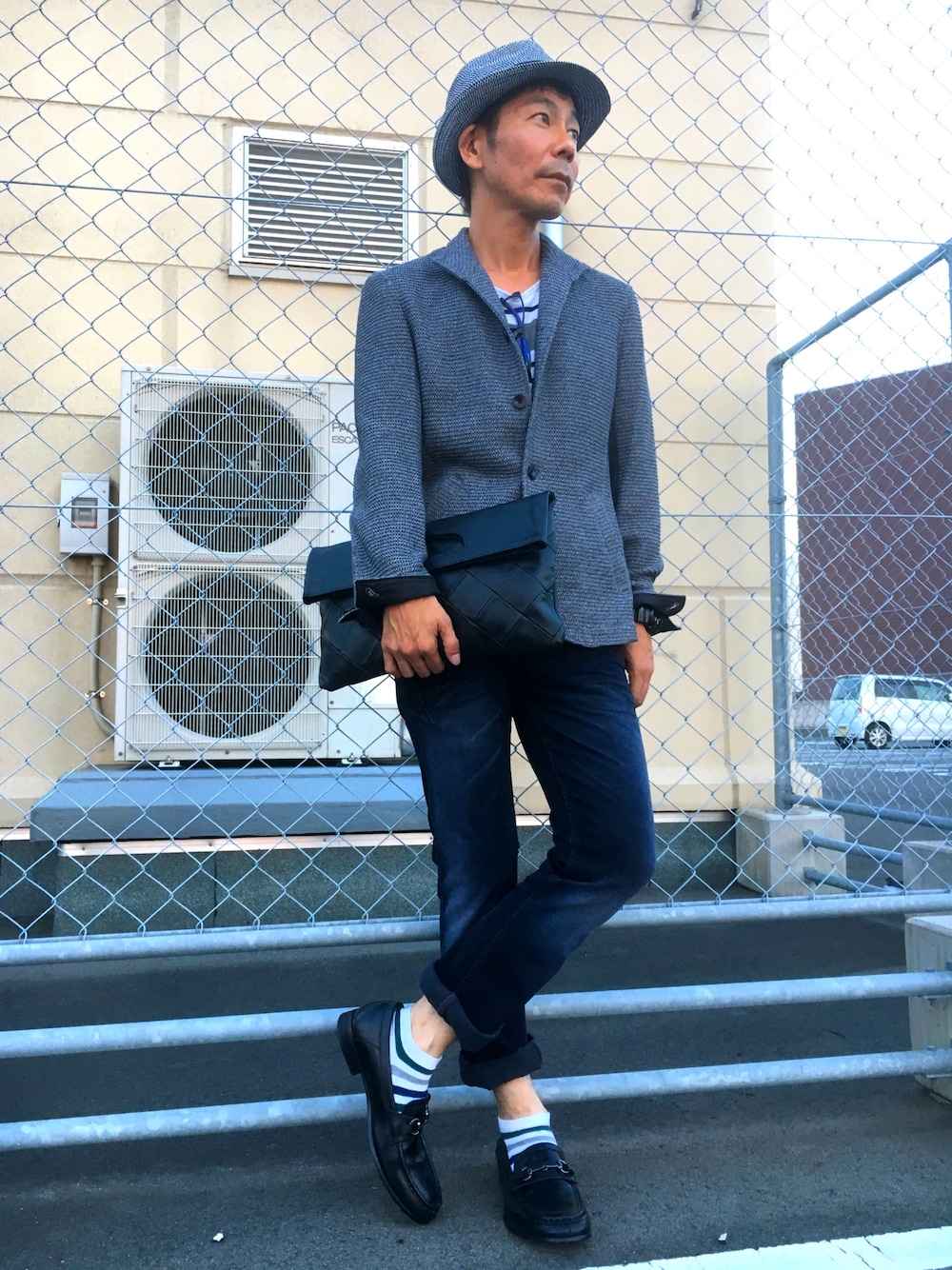 グレー系のテーラードジャケット、ブルー系のデニムパンツ、ブラック系のクラッチバッグを着用したメンズの夏コーディネートの1枚目の写真