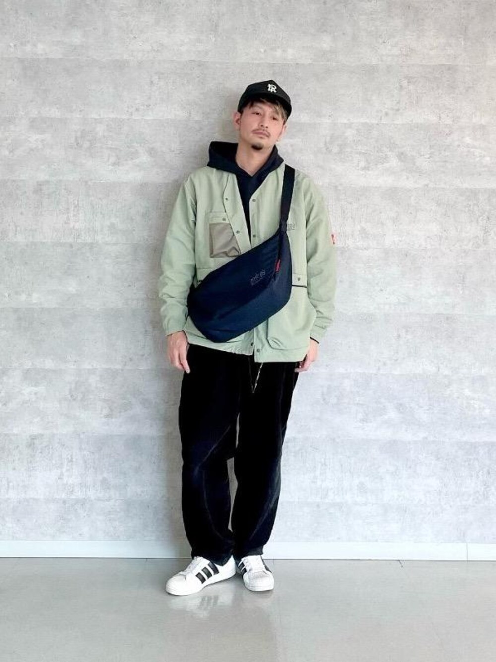 ブラック系のパーカー、ブラック系のショルダーバッグ、グリーン系のノーカラージャケットを着用したメンズの冬コーディネートの1枚目の写真