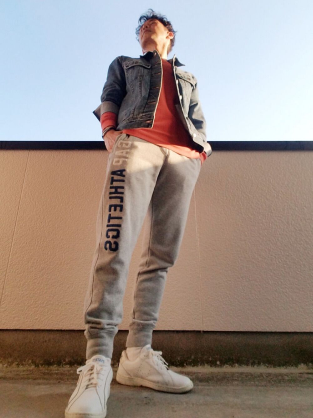 オレンジ系のTシャツ/カットソー、ブルー系のデニムジャケット、グレー系のスウェットパンツを着用したメンズの冬コーディネートの1枚目の写真