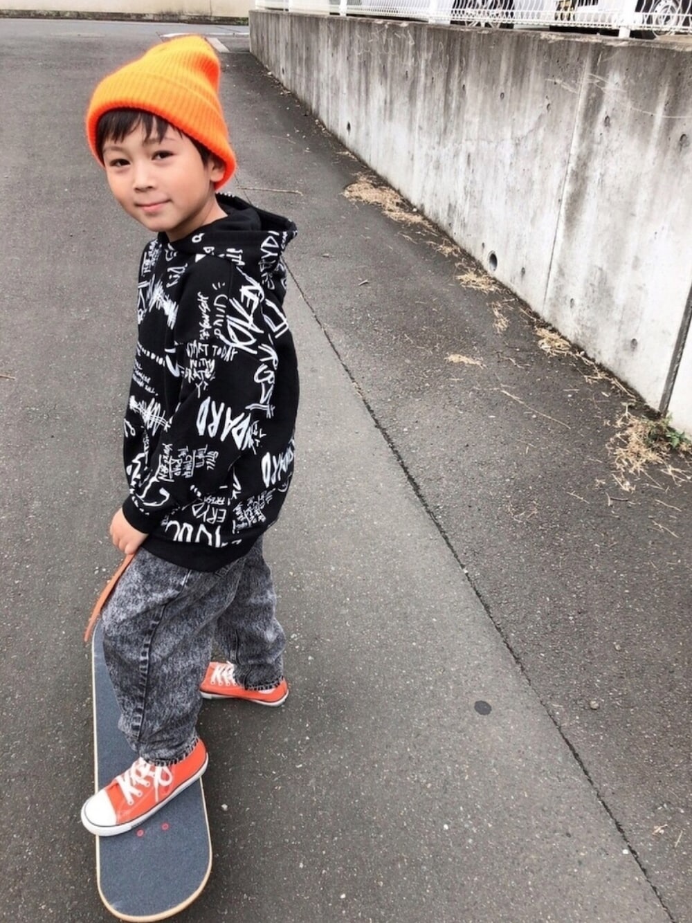ブラック系のパーカー、グレー系のデニムパンツ、オレンジ系のスニーカーを着用したキッズの秋コーディネートの1枚目の写真