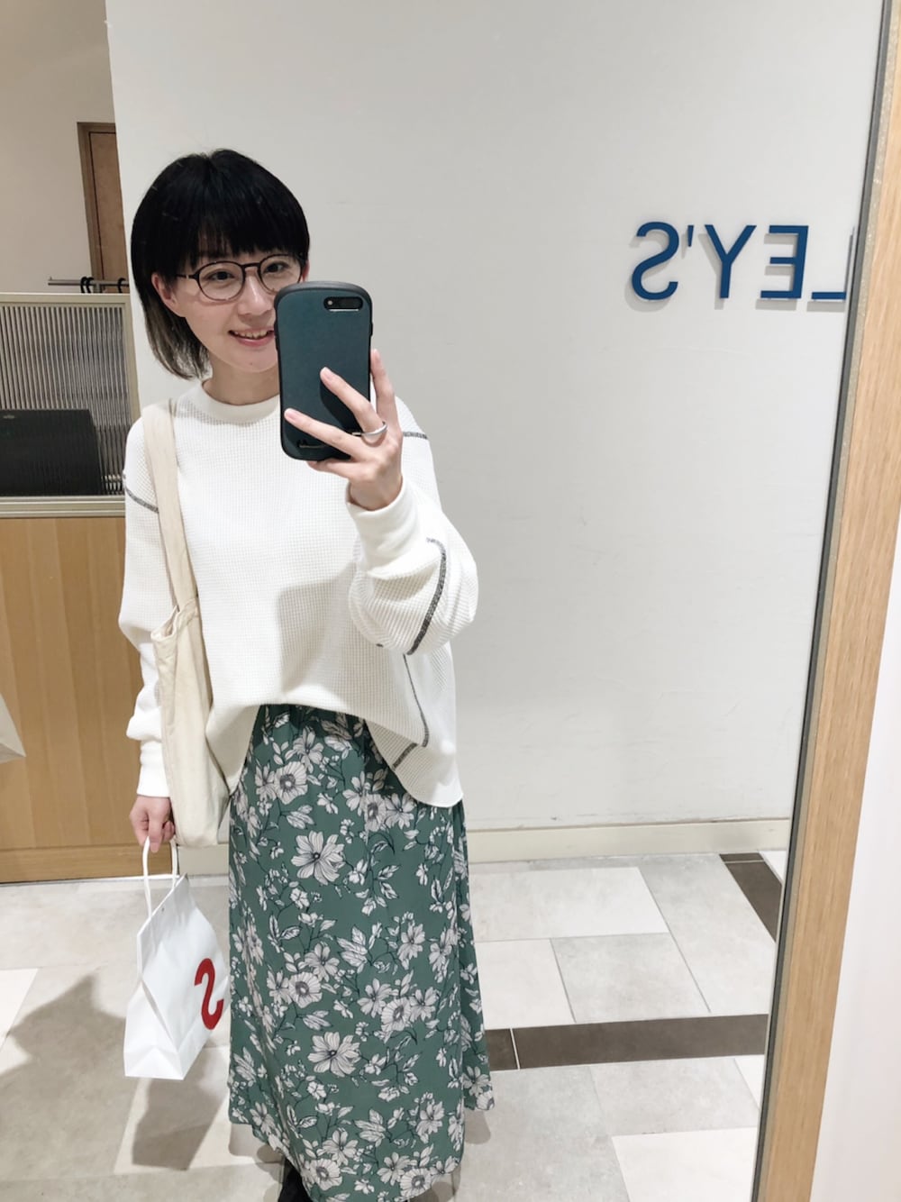 ホワイト系のTシャツ/カットソー、グリーン系のスカート、ブラック系のスニーカーを着用したレディースの春コーディネートの1枚目の写真