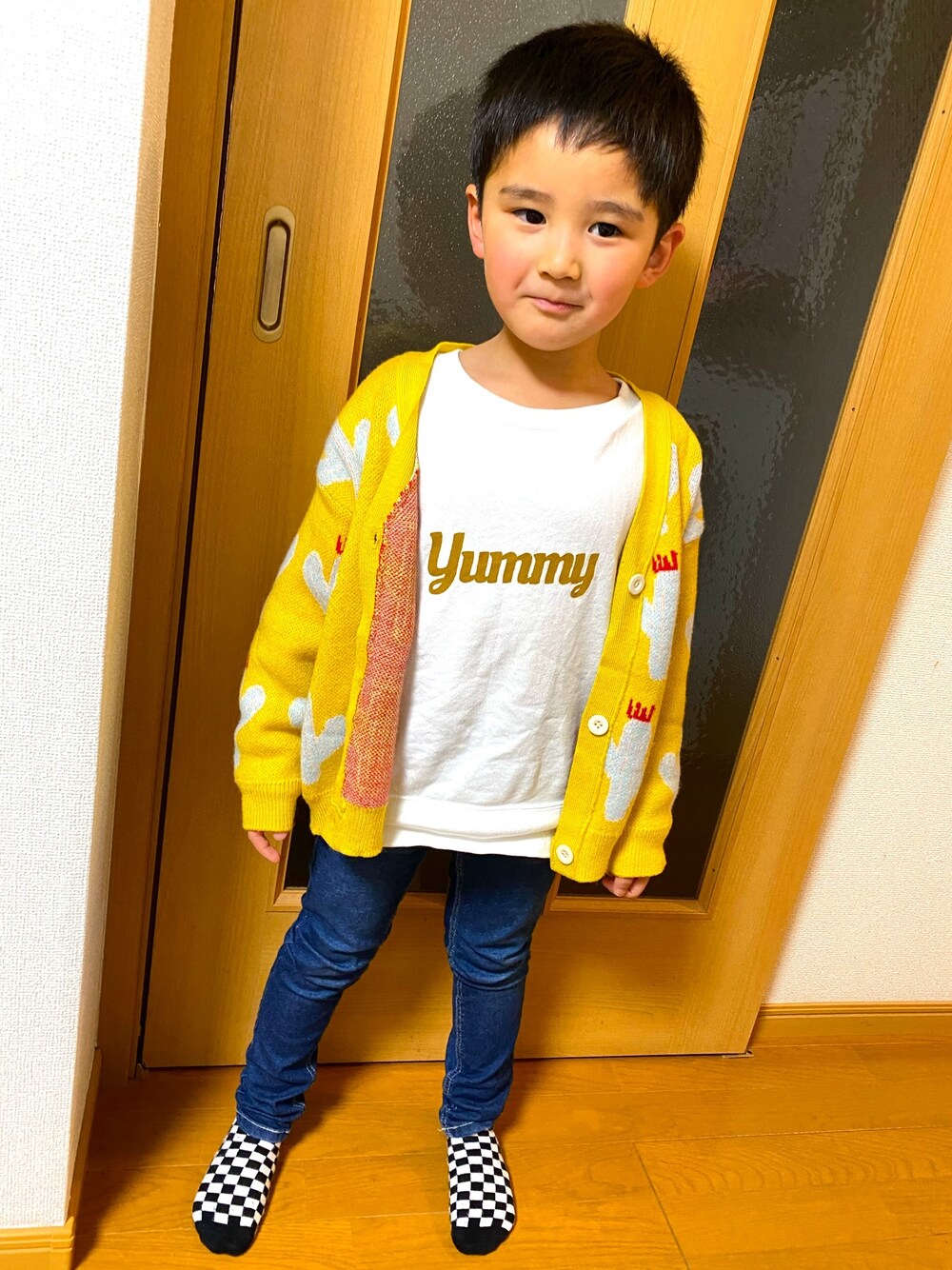 ホワイト系のスウェット、イエロー系のカーディガン/ボレロ、ブルー系のデニムパンツを着用したキッズの冬コーディネートの1枚目の写真