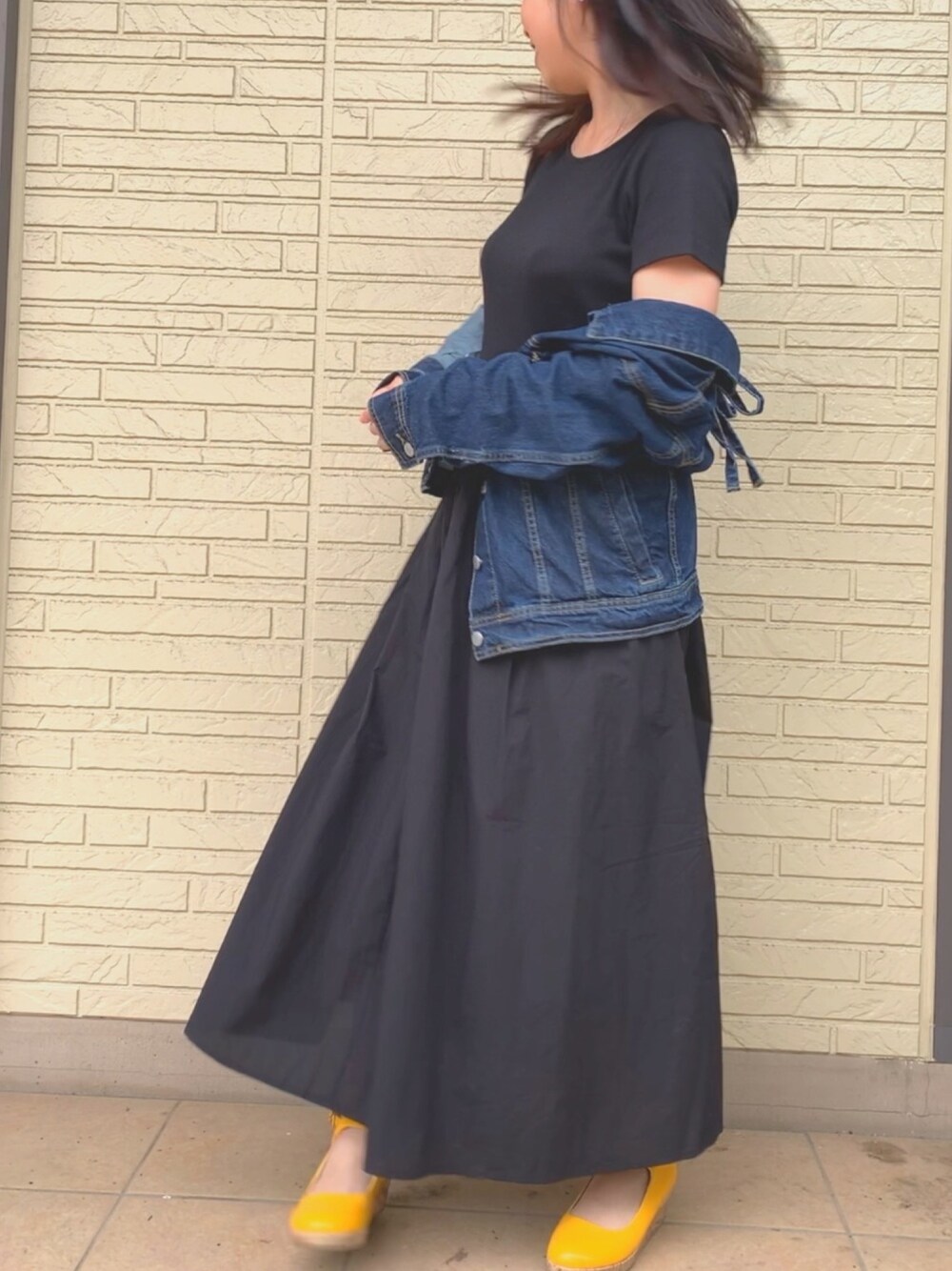 ブルー系のデニムジャケット、ブラック系のワンピース、イエロー系のパンプスを着用したレディースの春コーディネートの1枚目の写真